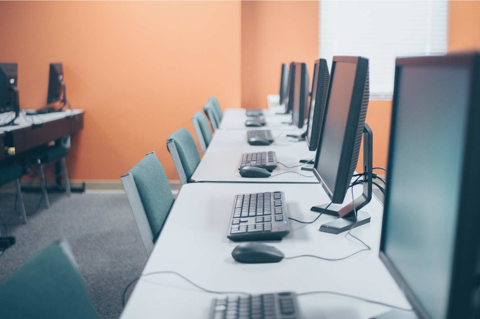 Multiple computers and computer screens with monitors, mouses and keyboards all sitting on a desk