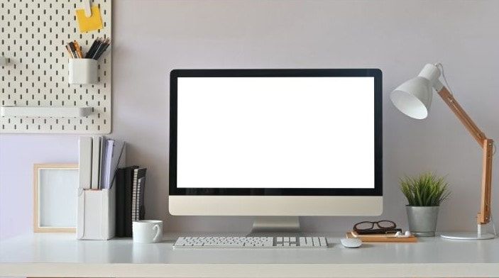 Home computer desk with computer, keyboard, lamps, tack board books and a green plant.