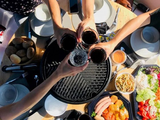 Mensen brengen een toast uit boven een ronde barbecue op een boot, met schalen vol eten eromheen.