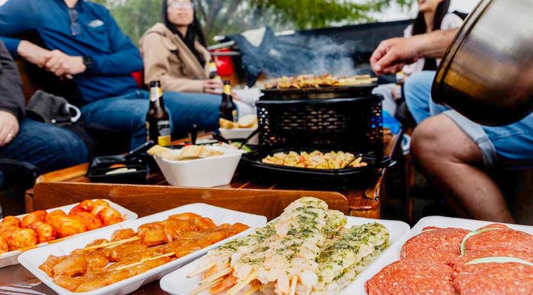 Buitenbarbecue met gegrilde vis en groenten, geserveerd op schalen rond een vuurkorf op een boot.
