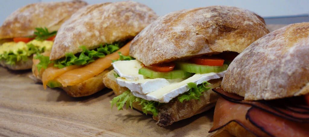 Diverse knapperige sandwiches met sla en tomaat, uitgestald op een houten plank op een boot.