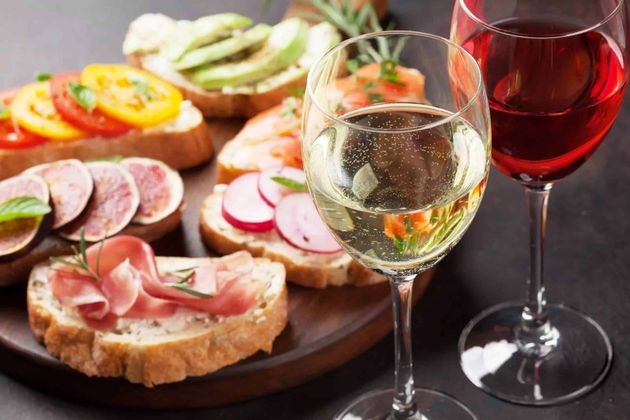 Wijnglazen naast een schaal met diverse hapjes en bruschetta op een donkere tafel.