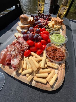 Borrelplank met prosciutto, tomaten, druiven, brood en dipsauzen. Buiten met flessen op de achtergrond.