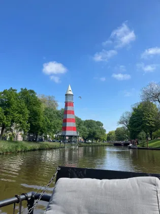 Een rood-wit gestreepte vuurtoren in een kanaalpark onder een helderblauwe hemel, gezien vanaf een bootstoel.