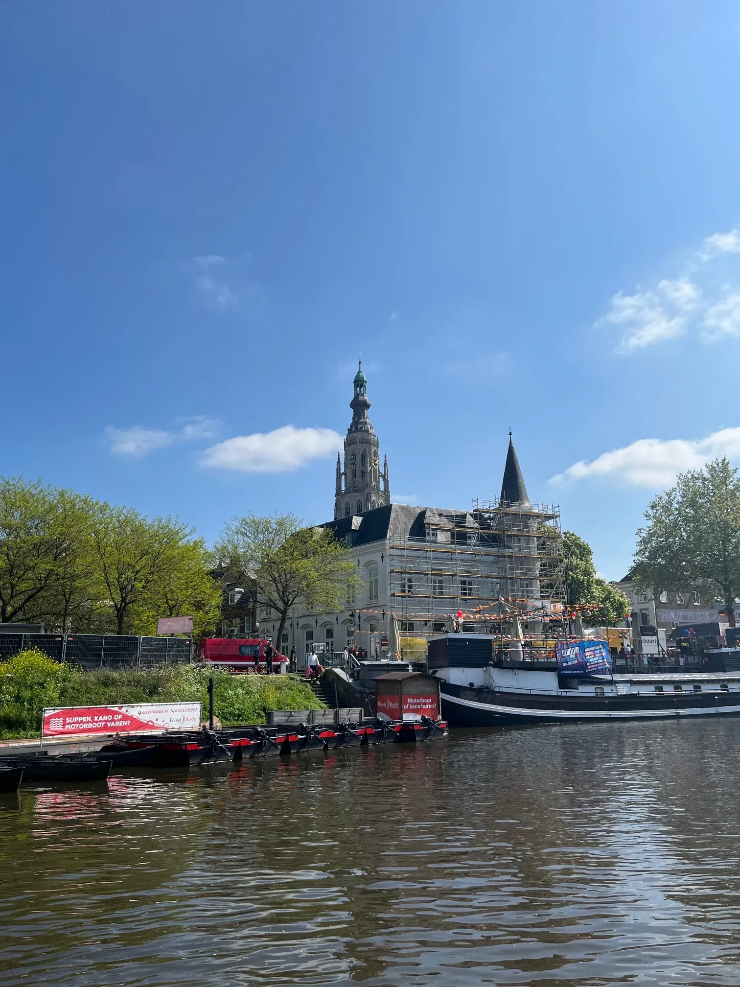 Historisch gebouw aan een kanaal met boten, bomen en een helderblauwe lucht.