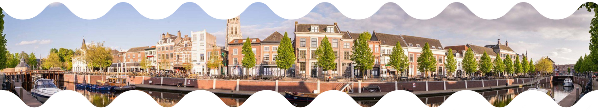 Panoramisch uitzicht op de stad Breda met gebouwen langs een waterweg, bomen en de lucht.