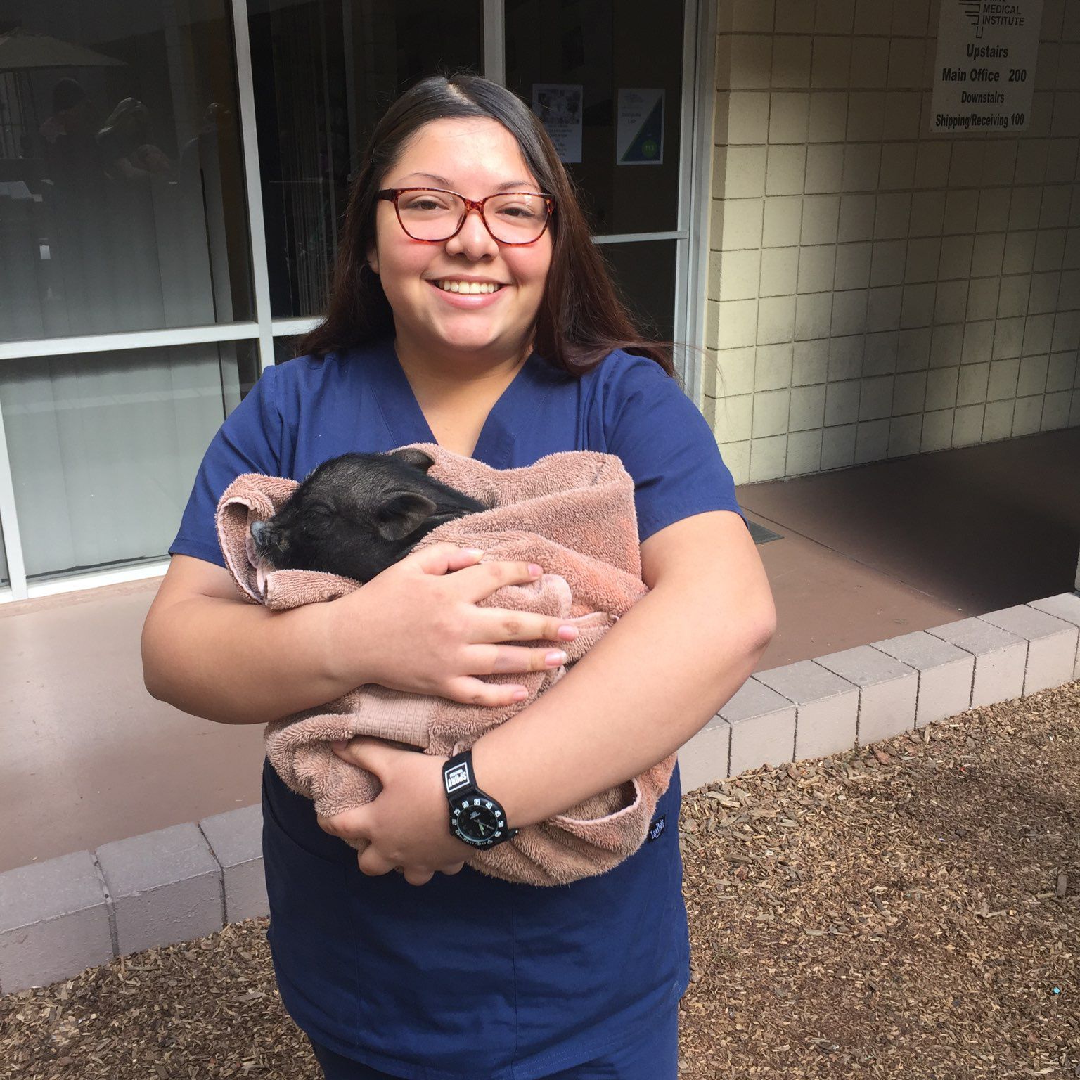 A woman wearing glasses is holding a small black animal wrapped in a towel.