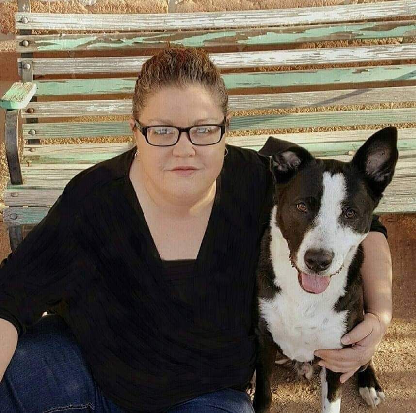 A woman wearing glasses is kneeling next to a black and white dog