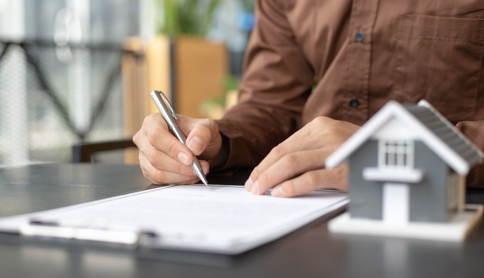 Person signing documents beside a small house model on a desk