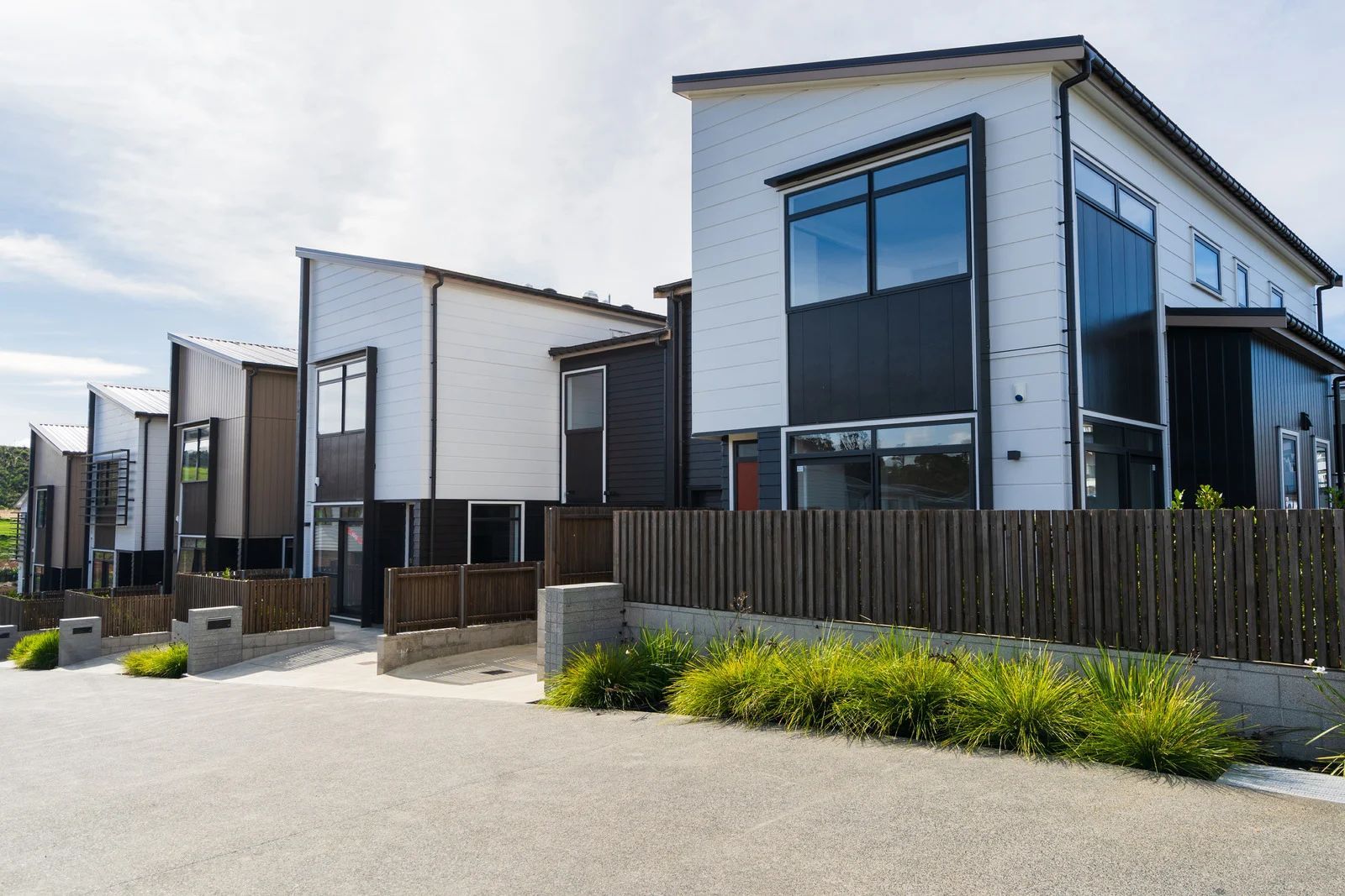 Modern row of white-and-black townhouses with fenced front yards under a clear sky