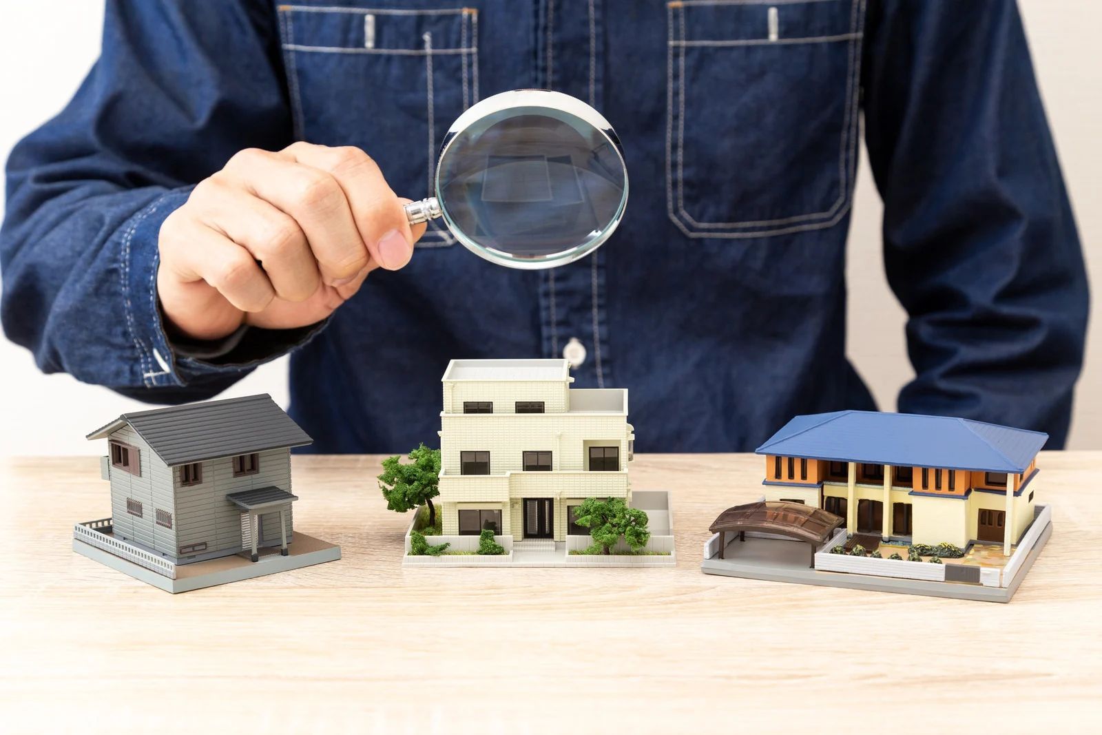 Person examining model houses with a magnifying glass on a table