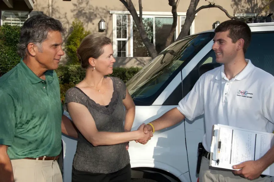 Couple shaking hands with service technician by van.