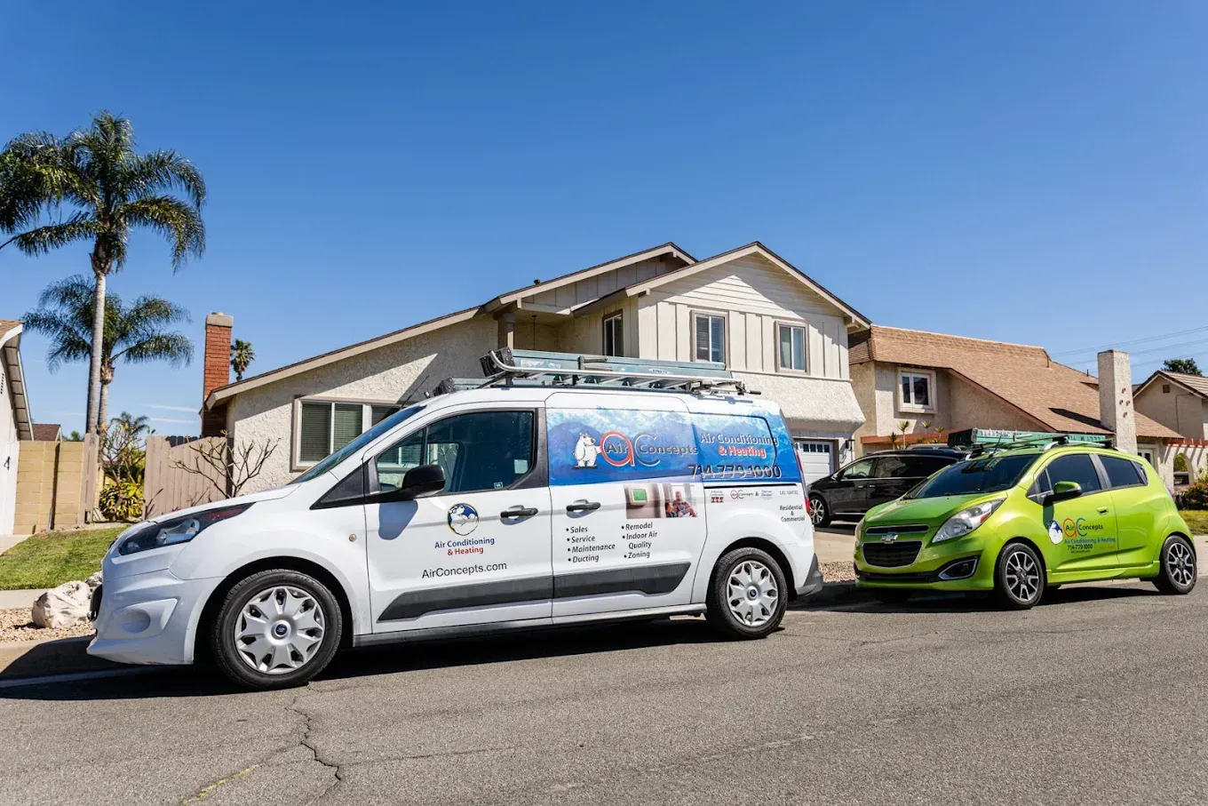 A white van and green car parked in a residential street on a sunny day.