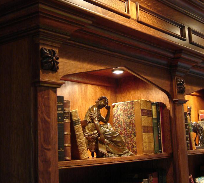 Wooden bookshelf with books and sculptures, lit by a small spotlight.