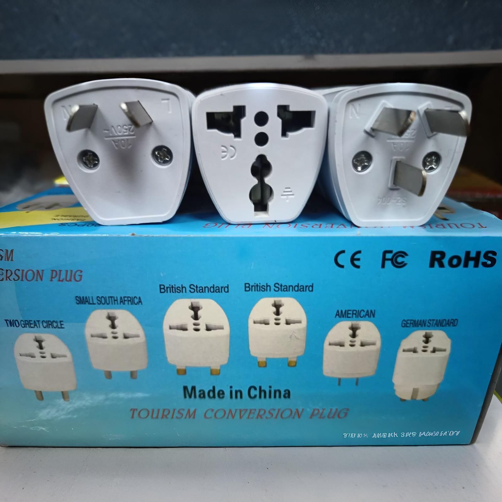 Tres enchufes adaptadores de viaje blancos en una caja azul, que muestran diferentes tipos de enchufes; 