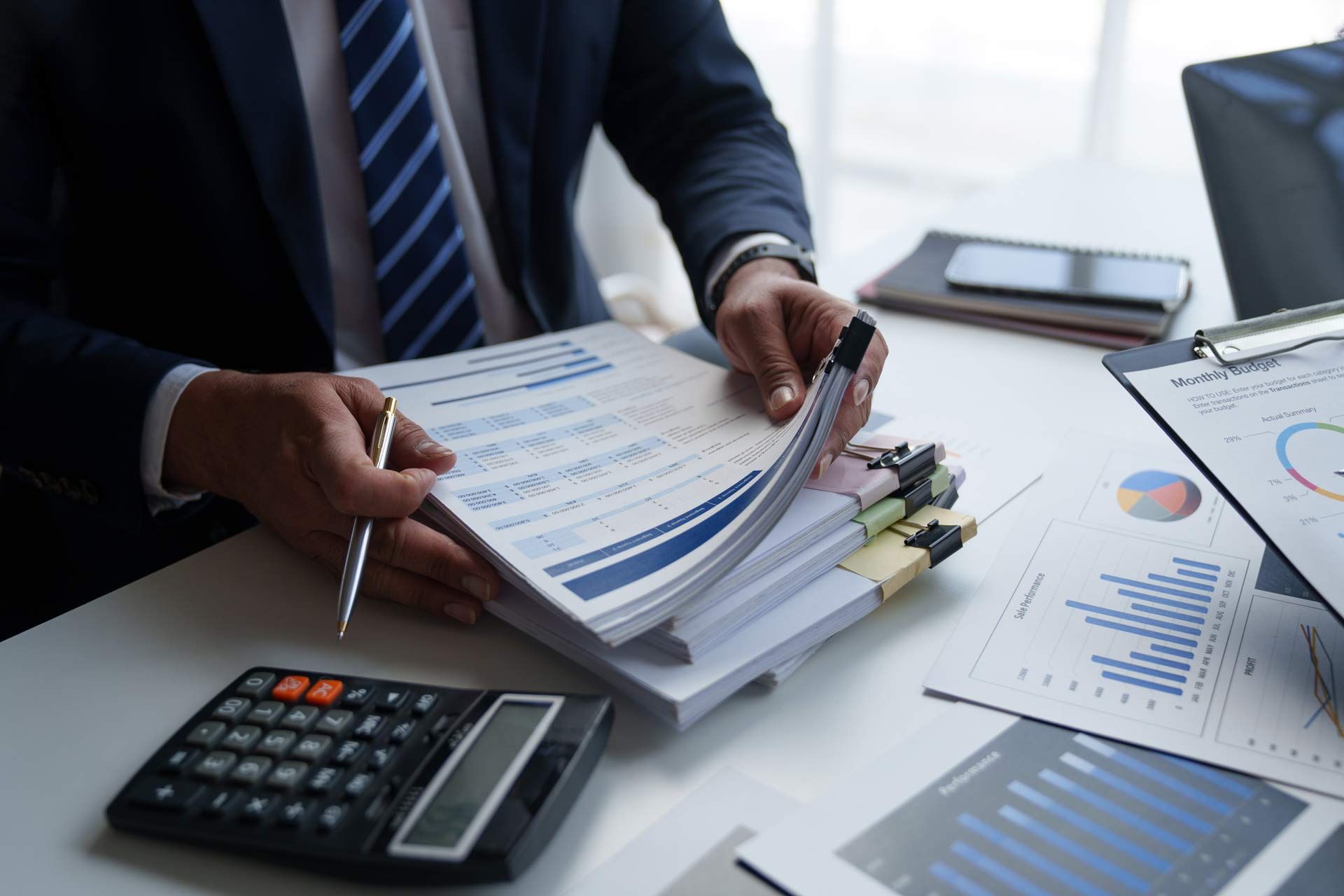 Person in suit reviews documents at a desk with a calculator and financial charts.