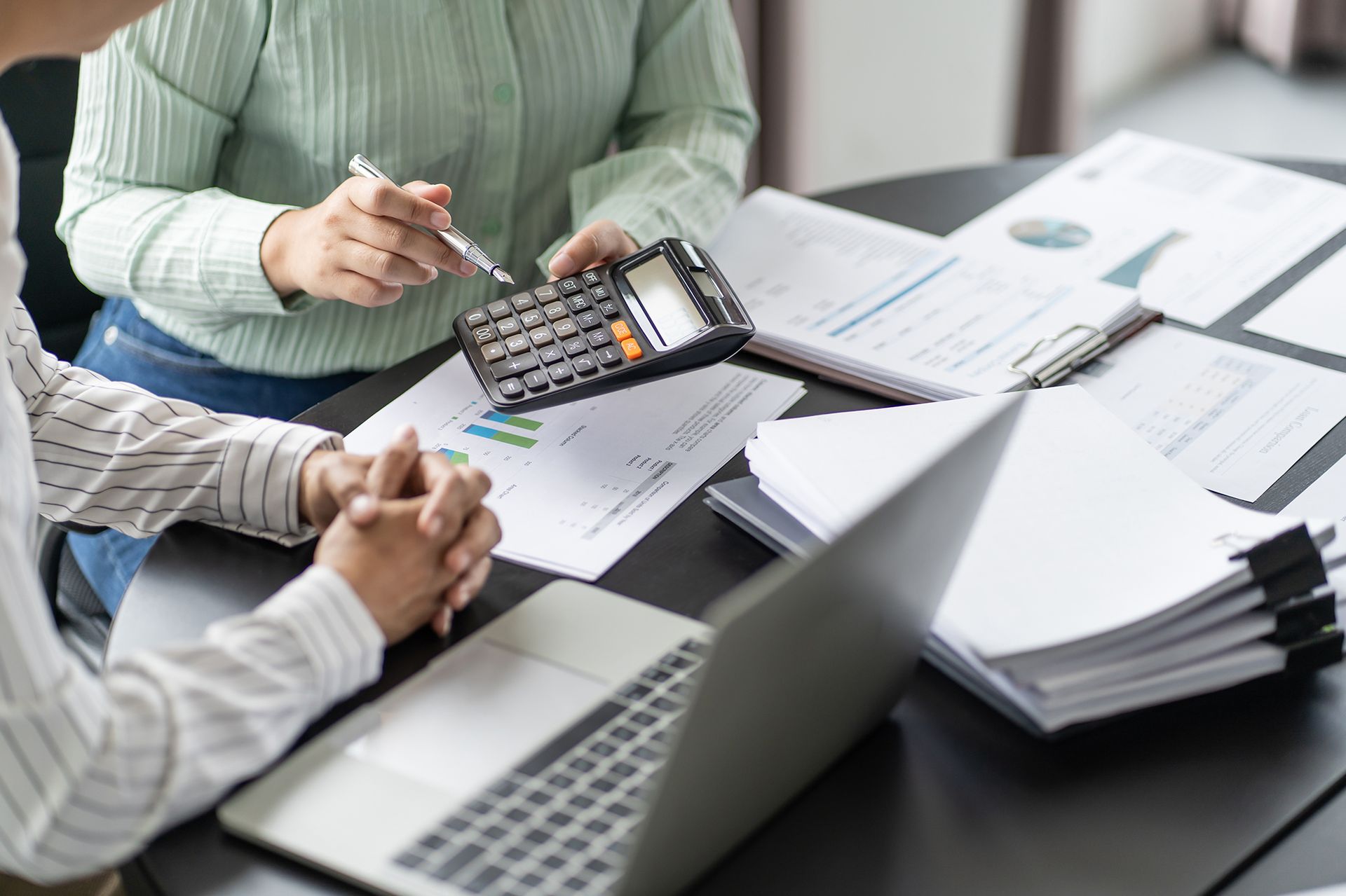 Two people reviewing financial documents, using a calculator and laptop at a desk.