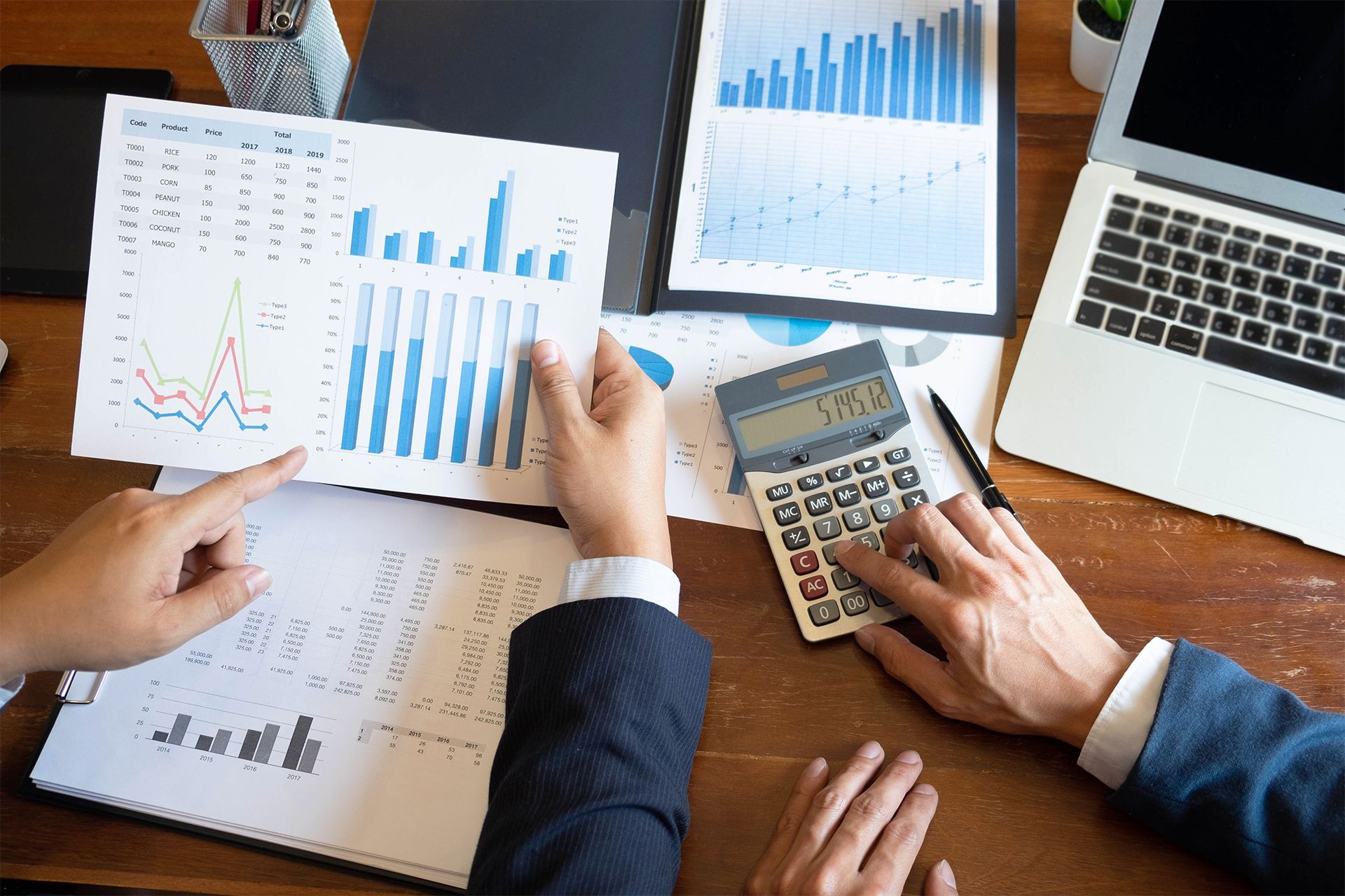Two people reviewing financial charts with a calculator and laptop on a desk.