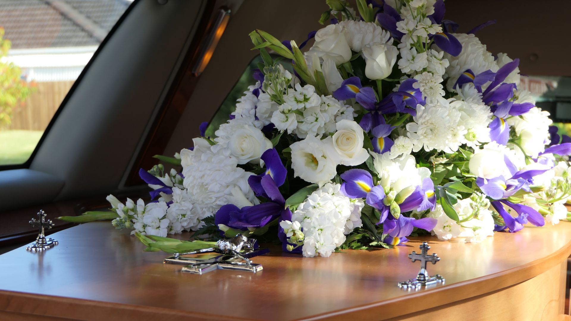 Composizione floreale di fiori bianchi e viola sopra una bara di legno all'interno di un carro funebre.