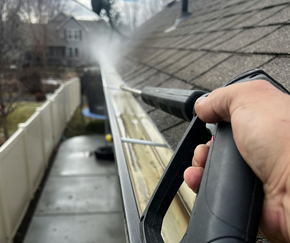 Person cleaning a gutter with a pressure washer; water spraying along the gutter.