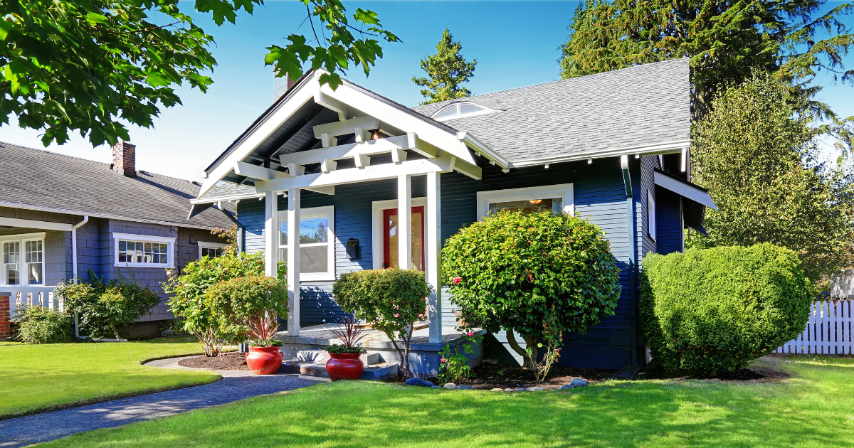 A blue house with a white porch is sitting on top of a lush green lawn.