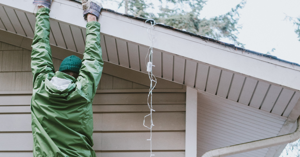 A man is hanging christmas lights on the roof of a house.