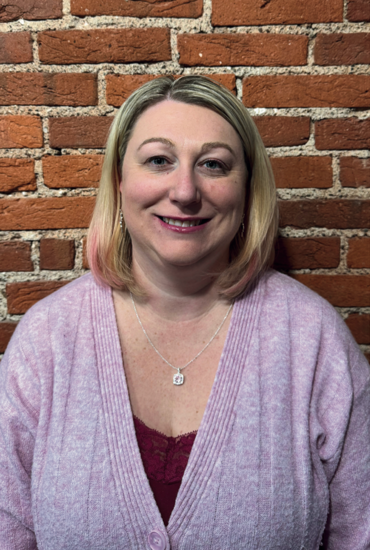 Woman in pink sweater smiling in front of a brick wall.
