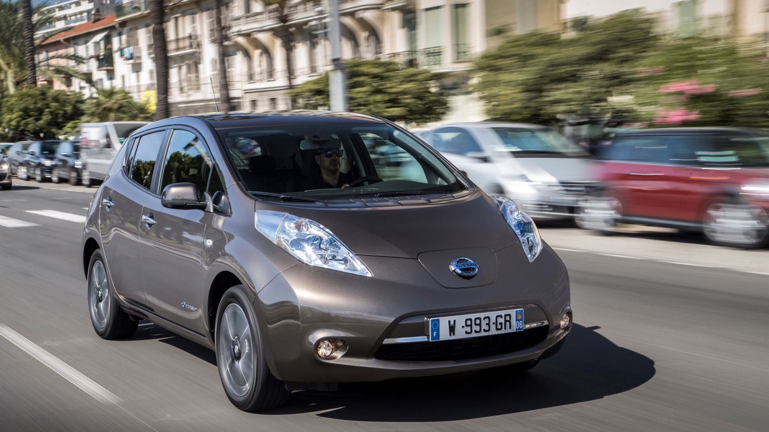 A Nissan leaf electric car is driving down a city street.