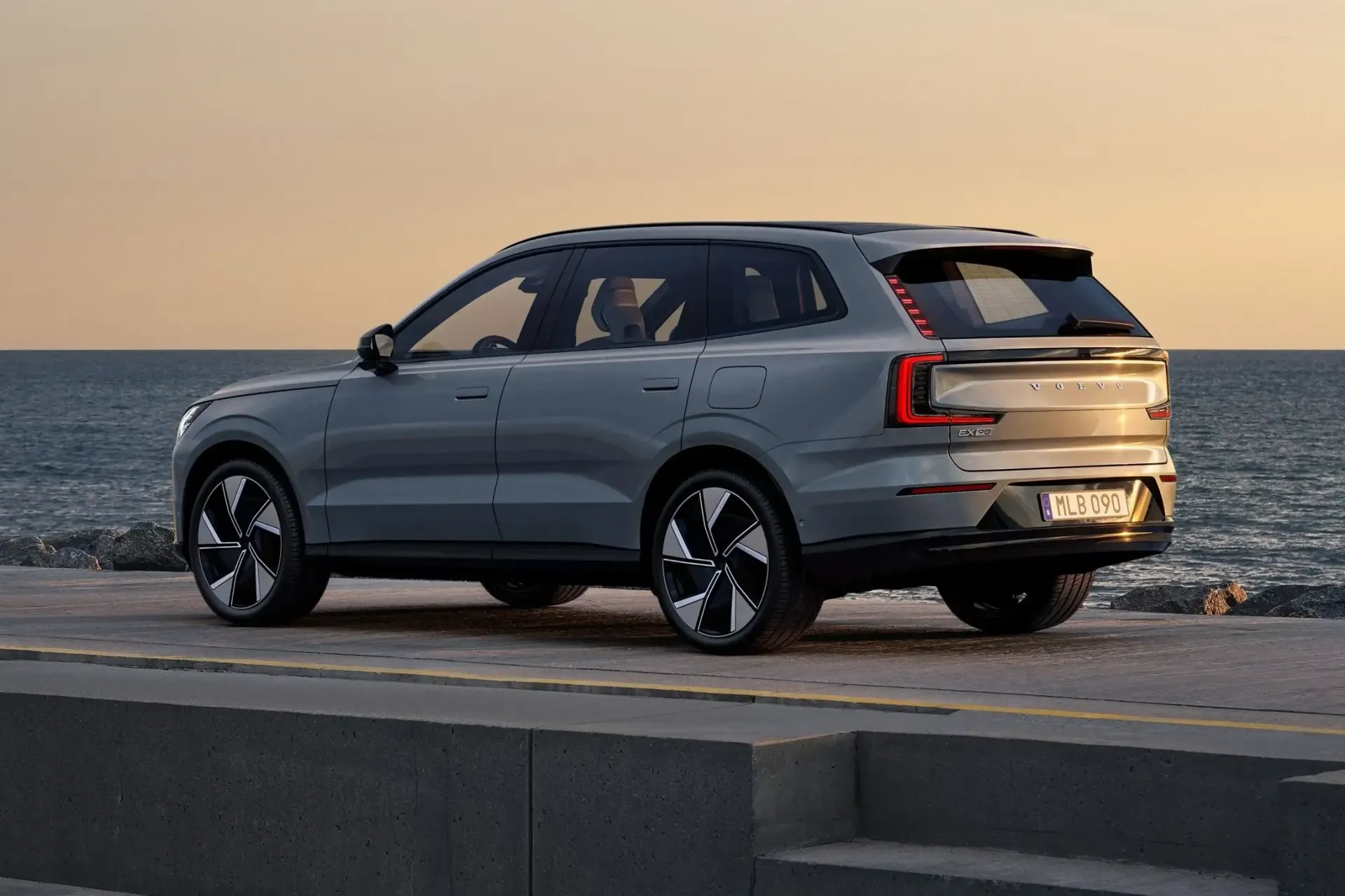 A volvo EX90 SUV is parked on a beach next to the ocean.