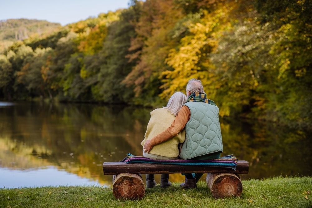 Couple sitting on a log bench, hugging, overlooking a lake with colorful autumn trees.