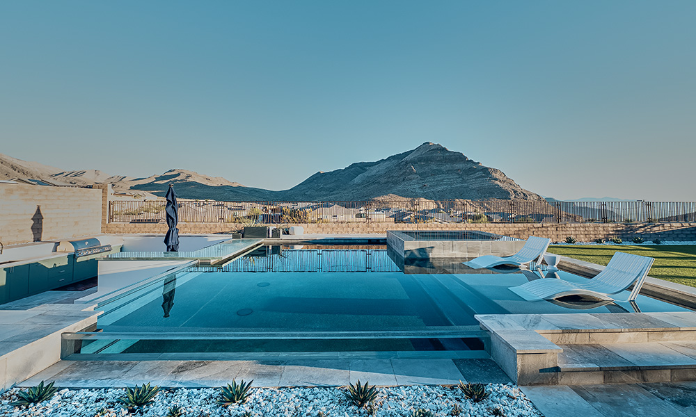 Modern rooftop pool with lounge chairs overlooking a mountain and waterfront at sunset