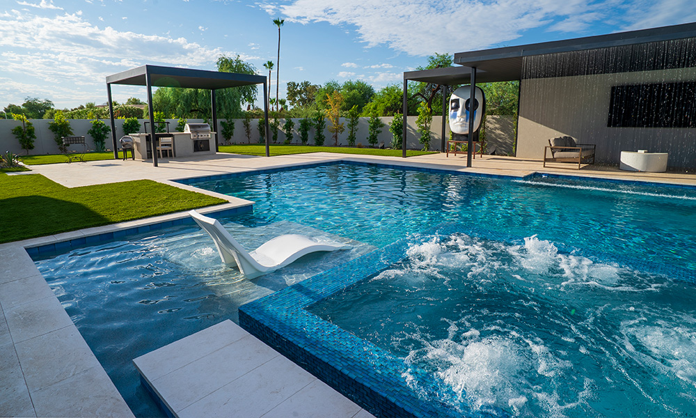 Modern backyard pool with lounge chairs, umbrella, and blue water splashing beside a small slide