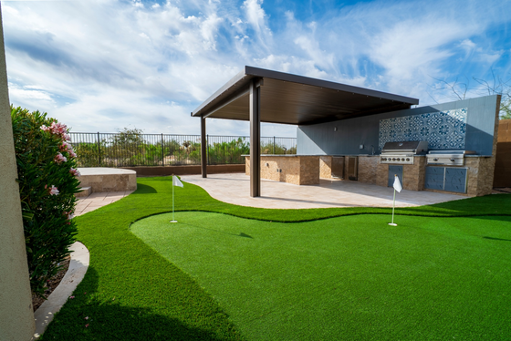 Modern playground with green artificial turf, shaded pavilion, and water play area under a blue sky