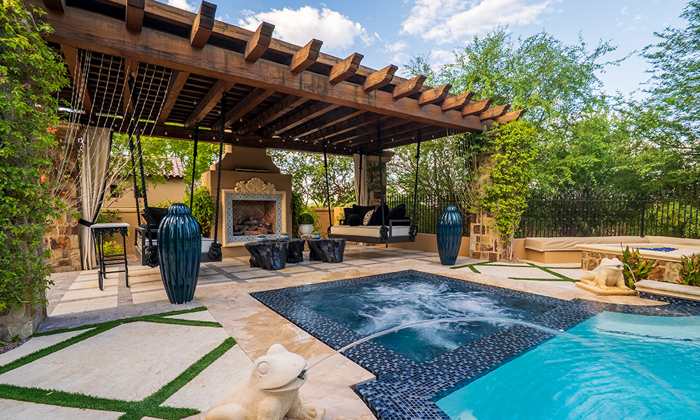 Backyard pool patio with a pergola, lounge chairs, and stone seating area under clear skies