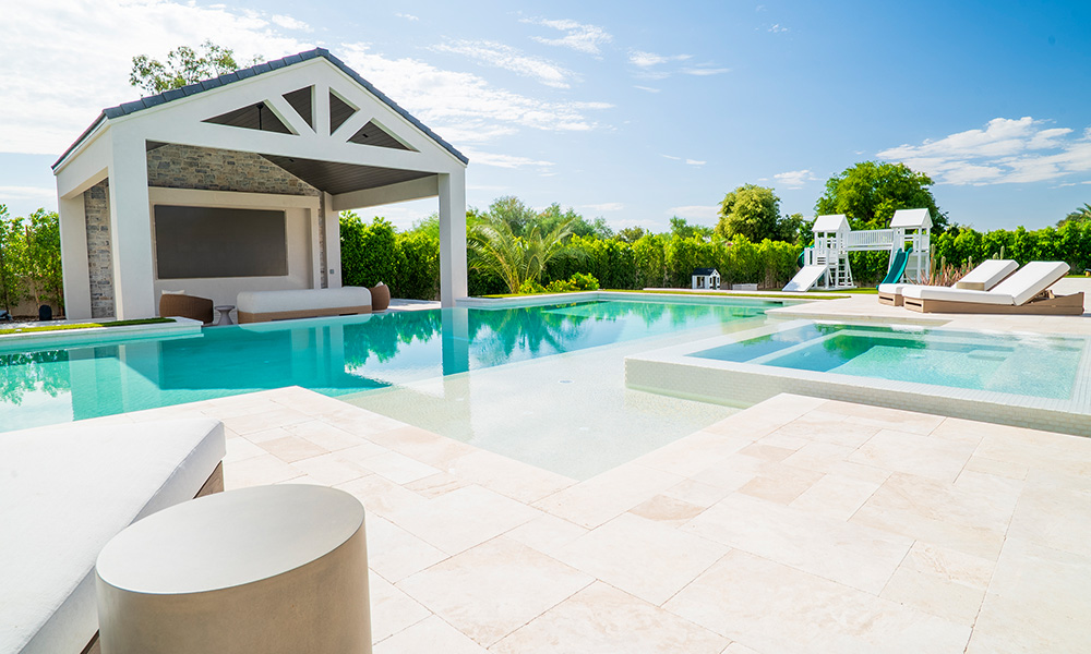 Modern backyard pool with a shaded cabana, lounge chairs, and bright blue water under a sunny sky