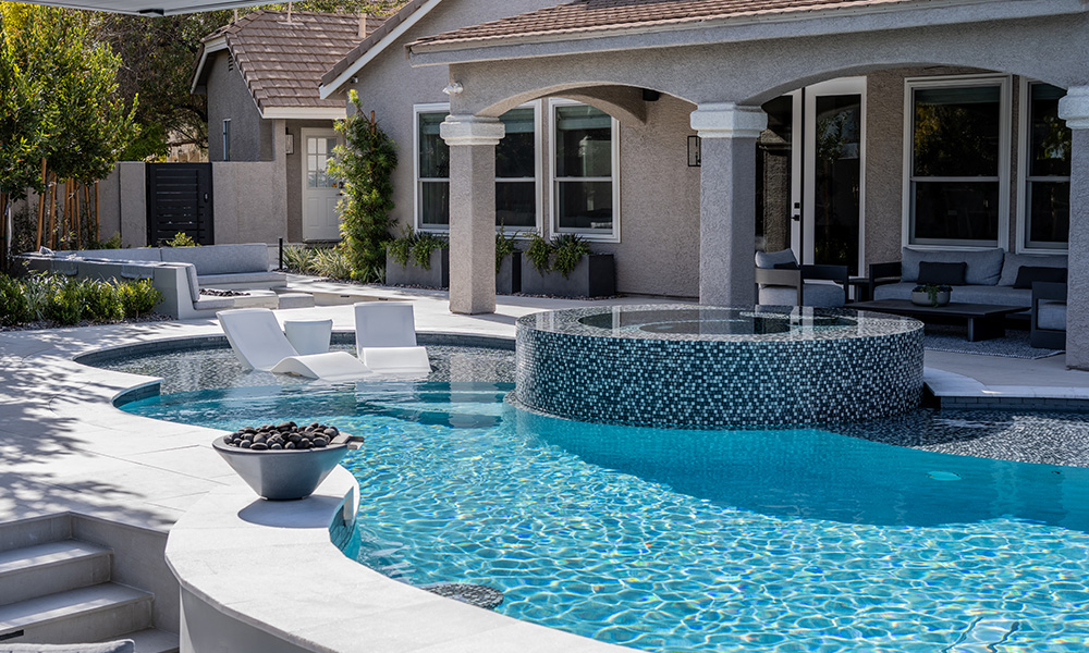 Backyard pool with curved spa, white lounge chairs, and a covered patio beside a house
