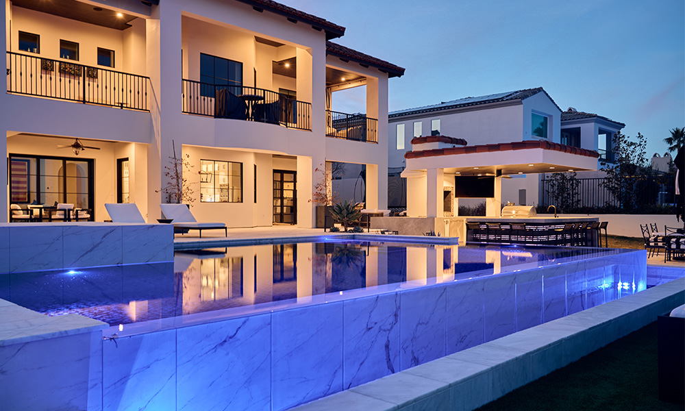 Luxury villa with lit balconies and a glowing blue infinity pool at dusk