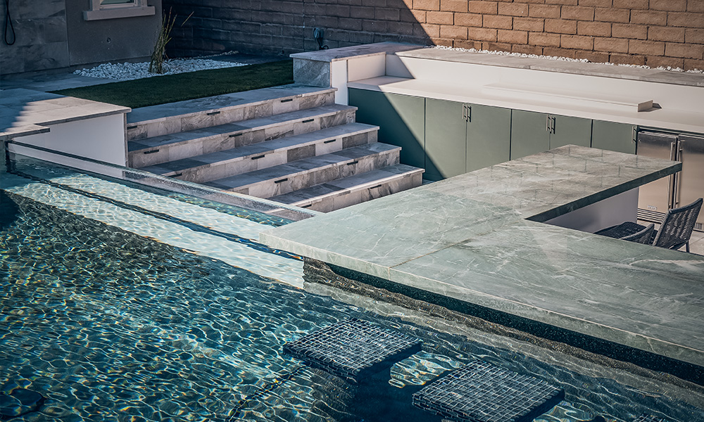 Backyard pool with stone steps, tiled water edge, and a raised patio beside it
