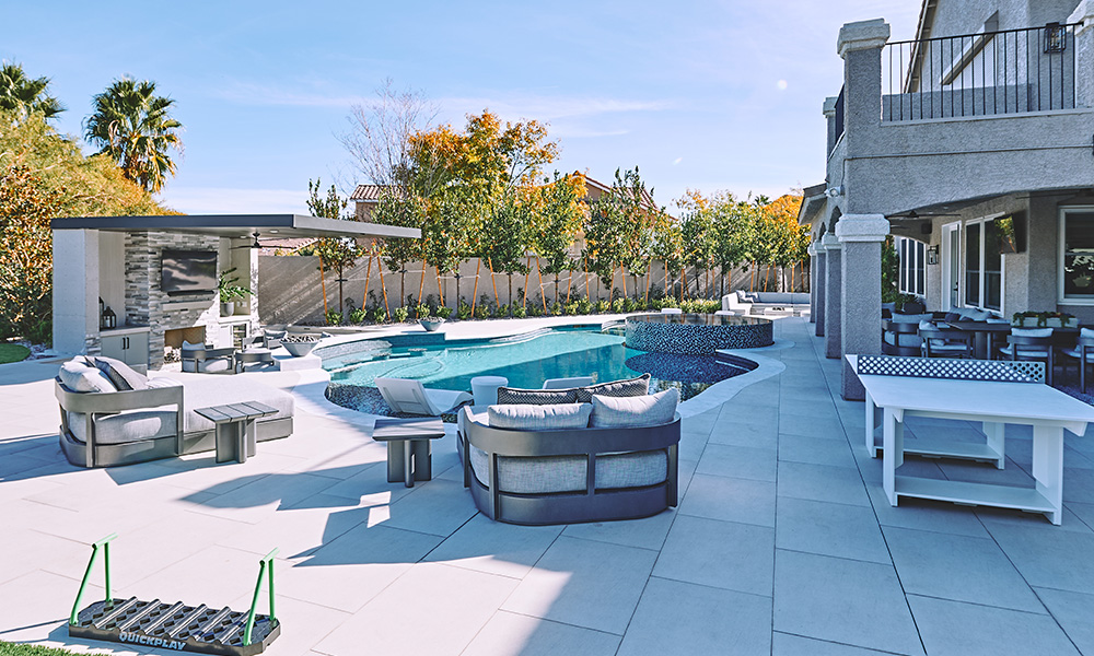 Modern backyard patio with a pool, cushioned seating, and a pergola in bright daylight