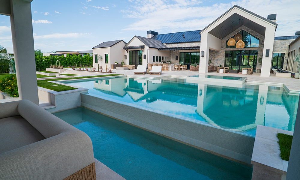 Modern luxury home with a large turquoise pool and patio seating under a bright blue sky