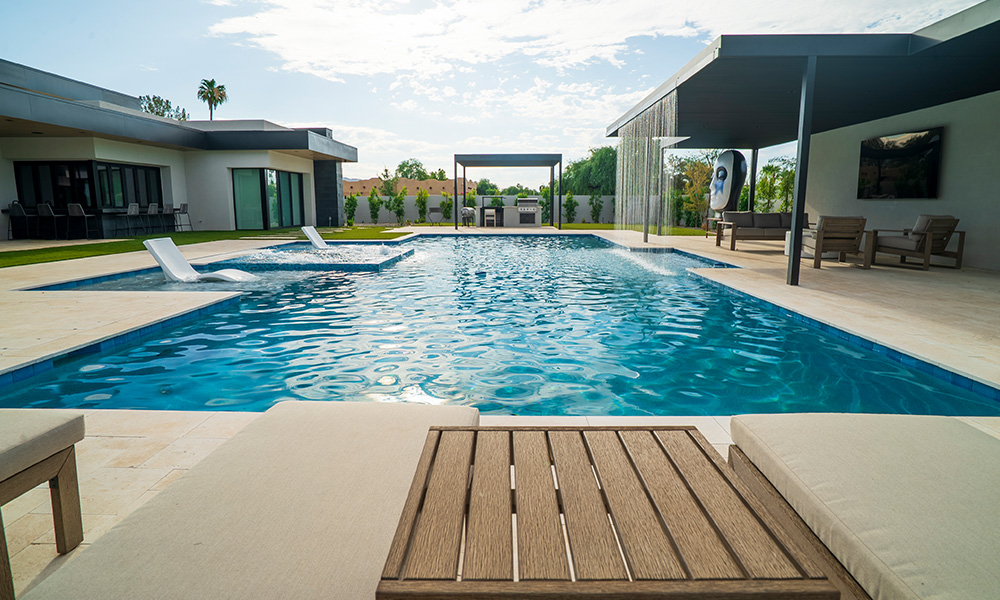 Modern outdoor swimming pool with blue water, white buildings, and lounge chairs on a sunny patio