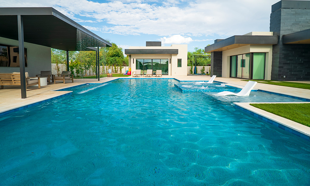 Luxury backyard pool with turquoise water, white lounge chairs, and modern home patio.