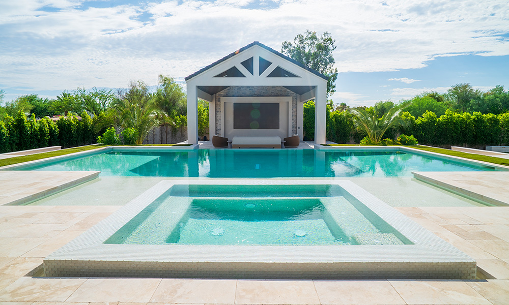 Modern backyard pool with white pavilion and turquoise water, surrounded by greenery and blue sky