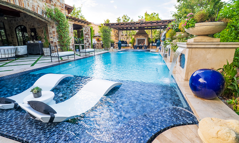 Elegant outdoor swimming pool with lounge chairs, blue sphere, and stone patio under a pergola