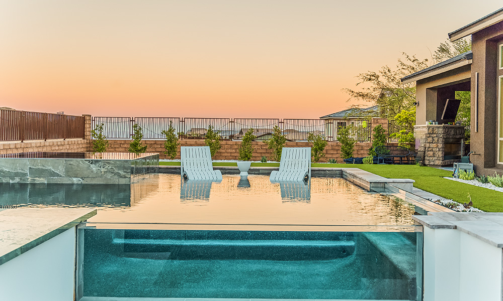 Modern backyard pool with two lounge chairs at sunset, patio, and landscaped yard