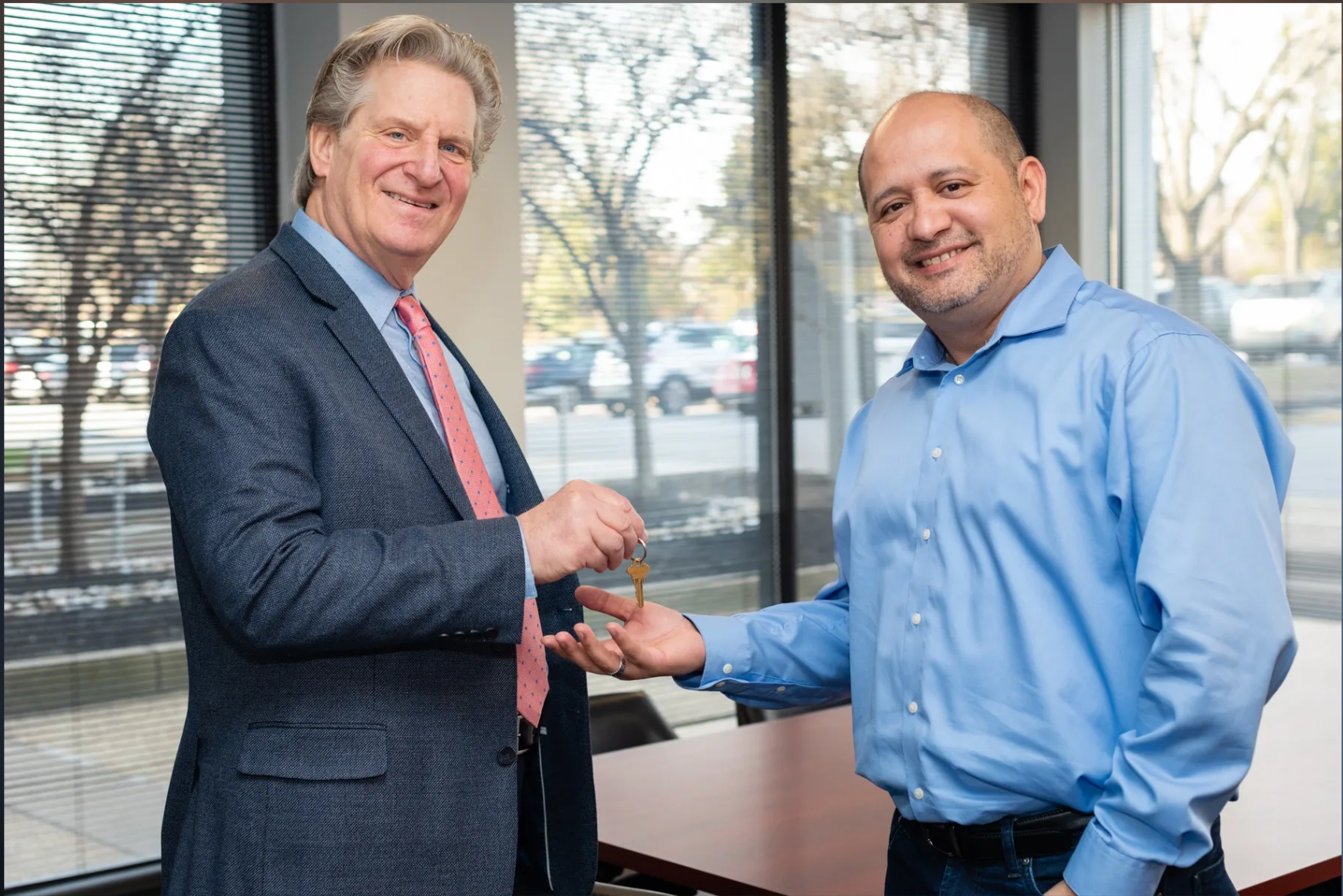 A man in a suit and tie is handing a key to another man