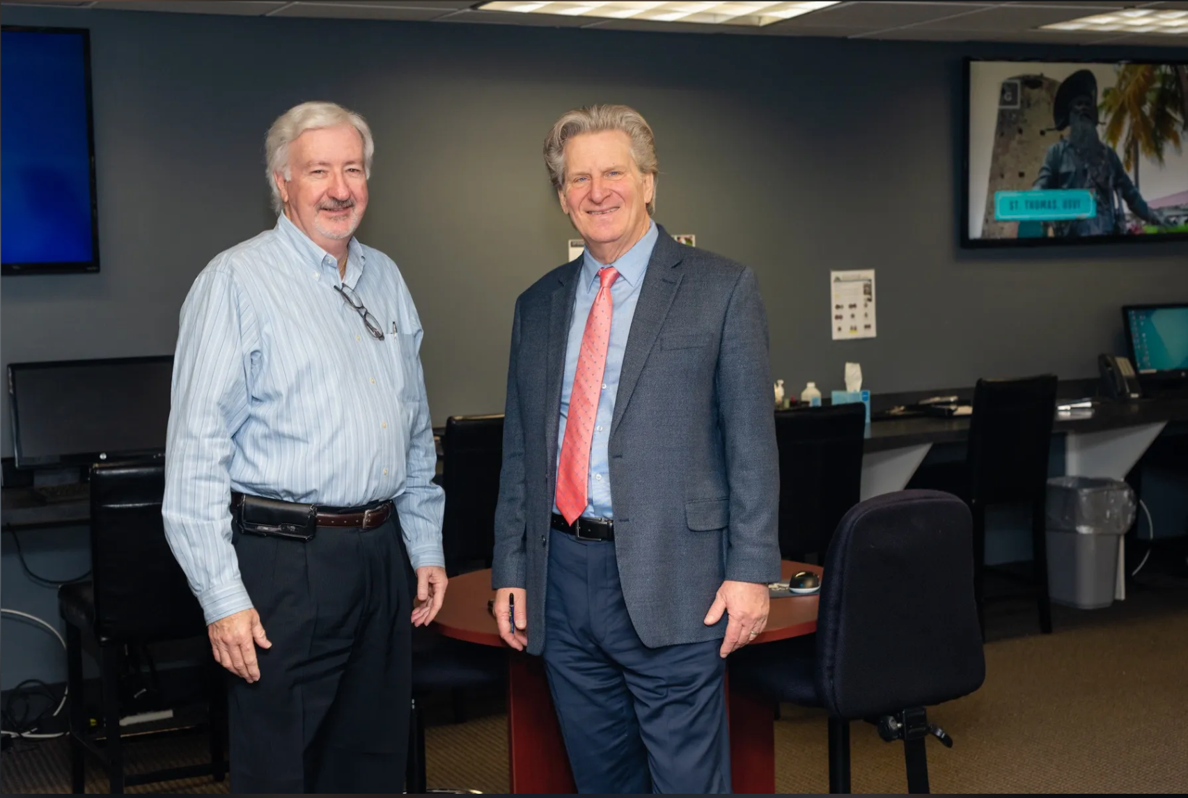 Two men in suits and ties are standing next to each other in an office.