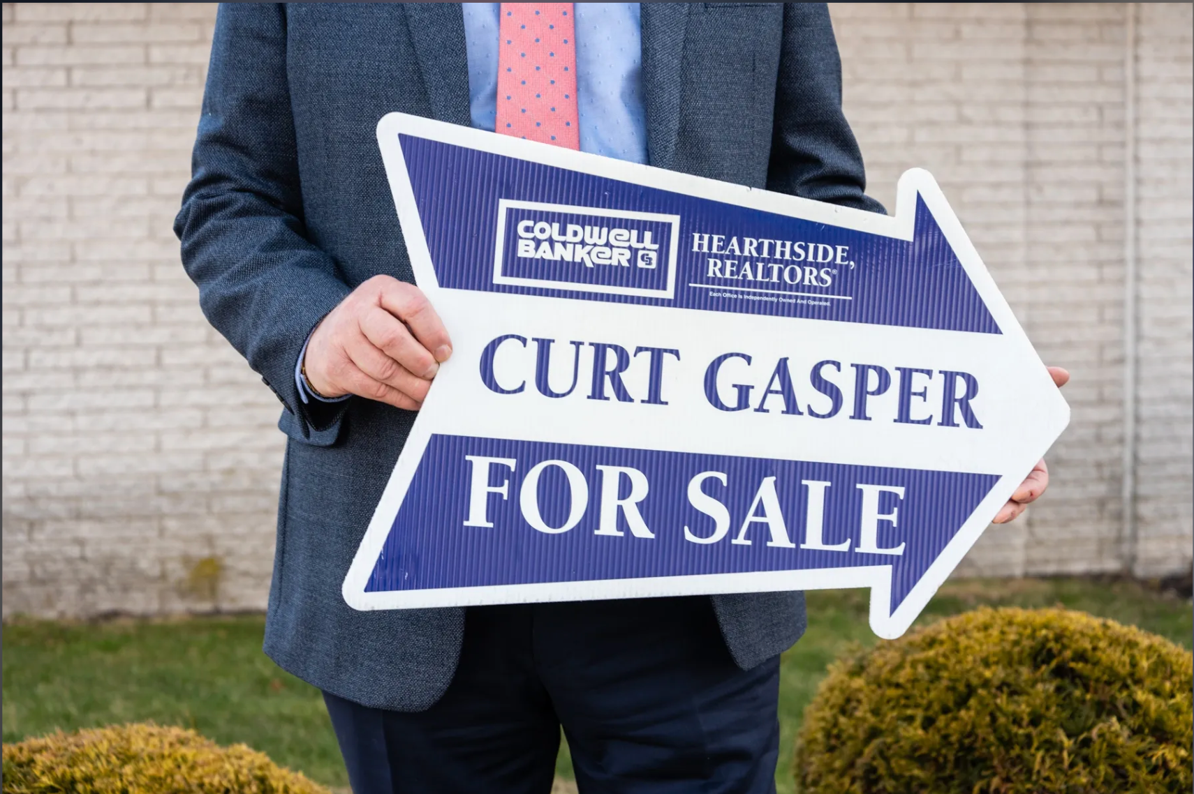A man in a suit and tie is holding a for sale sign.