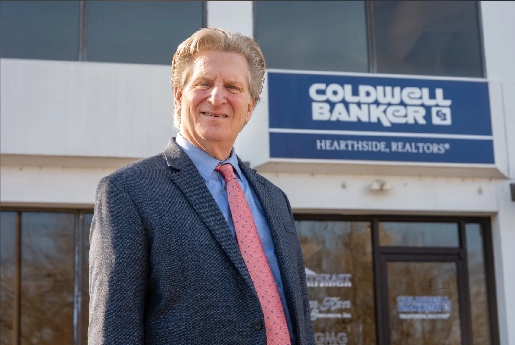 A man in a suit and tie is standing in front of a coldwell banker building