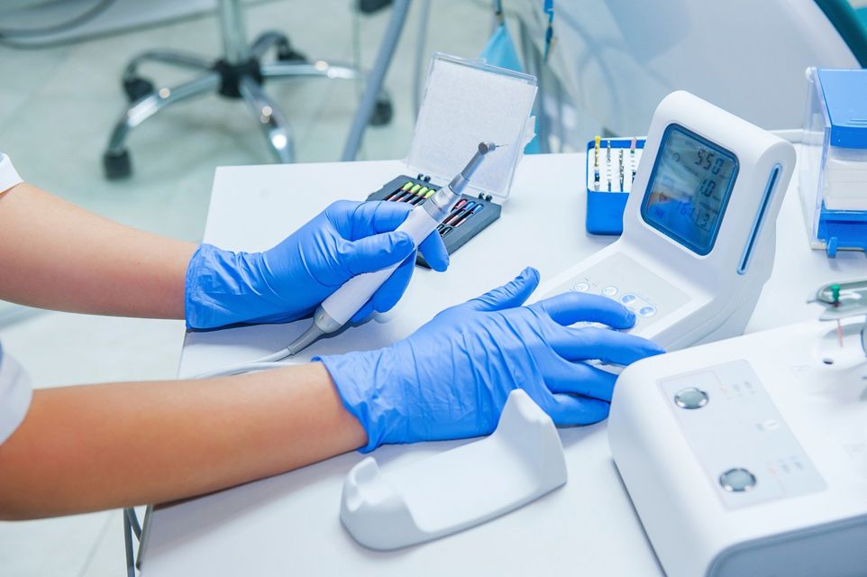 Mani guantate di blu che utilizzano uno strumento odontoiatrico su un dispositivo bianco da clinica posizionato su un bancone.